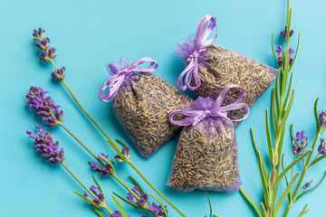 Fragrant bag or pouch with dried lavender flowers on blue background. Sprigs of lavender near the...