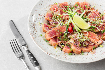 Close up of rare seared tuna slices with lime and arugula leaves on a plate. Gray background. Tuna salad. Top view from above horizontal.