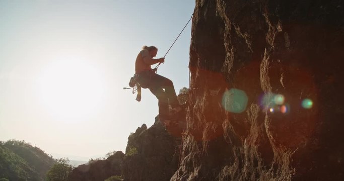 Professional caucasian alpinist is going down the cliff during sunset, using special ropes - extreme tourism concept 4k footage