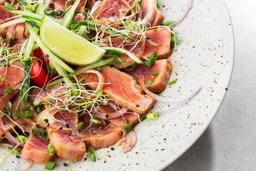 Close up of rare seared tuna slices with lime and arugula leaves on a plate. Gray background. Tuna salad. Top view from above horizontal.