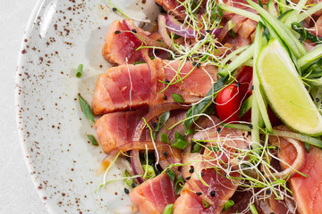Close up of rare seared tuna slices with lime and arugula leaves on a plate. Gray background. Tuna salad. Top view from above horizontal.