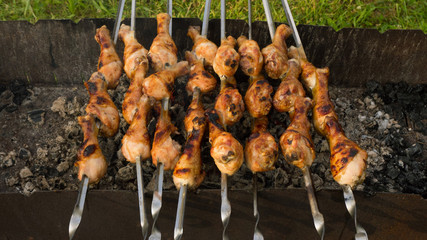 Close-up of grilled chicken legs on metal skewers, prepared on charcoal outdoors, horizontal image