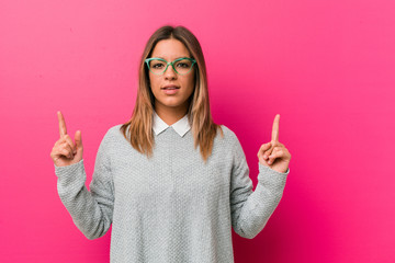Young authentic charismatic real people woman against a wall indicates with both fore fingers up...