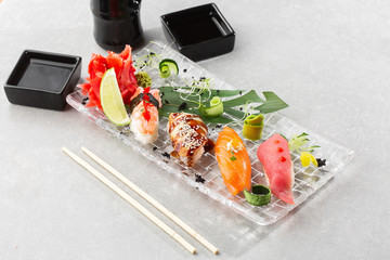 Nigiri sushi with salmon, eel, tuna and prawn, served on transparent plate. Delicious traditional Japanese food, tasty seafood, restaurant concept, food background. horizontal photo