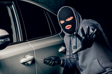 A man with a Balaclava on his head tried to break into the car. He uses a screwdriver. Hijacker, the concept of car theft.