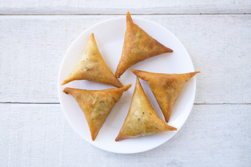 Samosas on white plate on white wood.Top view.