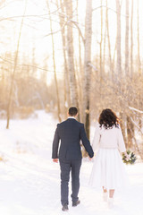 Beautiful wedding couple. Winter wedding of the groom in a beautiful suit and the bride in a beautiful wedding dress. Winter photo shoot newlyweds.