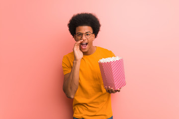 Young african american holding a popcorn bucket shouting something happy to the front