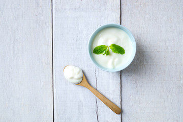 Top view of white yogurt on bluesky cup and wooden spoon on white wood.