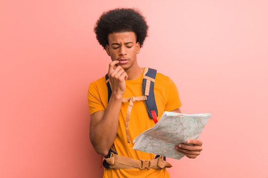 Young african american explorer man holding a map relaxed thinking about something looking at a copy space