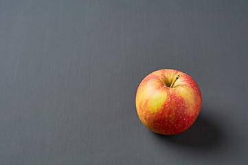 Single red fresh whole ripe apple full of vitamins lies on old dark scratched concrete table on kitchen. Harvest or diet concept. Space for text