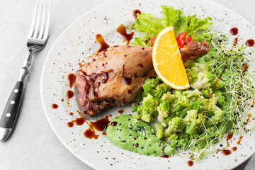 Roast duck leg with baked romanesco broccoli, lemon slice and chilli pepper on white plate, closeup. Horizontal view from above, top shot