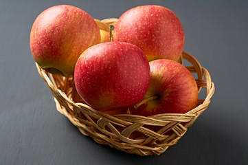 Lot of red fresh whole ripe apples full of vitamins lies in wooden wicker basket and old dark scratched concrete table on kitchen. Harvest or diet concept