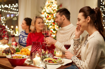 holidays, communication and celebration concept - happy young woman calling on smartphone and having christmas dinner with friends at home