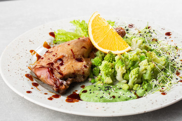 Roast duck leg with baked romanesco broccoli, lemon slice and chilli pepper on white plate, closeup. Horizontal view from above, top shot