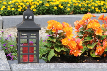 Grablaterne auf einem Friedhof, im leicht unscharfen Hintergrund zwei mit Sommerblumen bepflanzte...