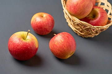 Three red fresh whole ripe apples with vitamins on background of full wooden wicker basket and old dark scratched concrete table on kitchen. Harvest or diet concept. Close-up