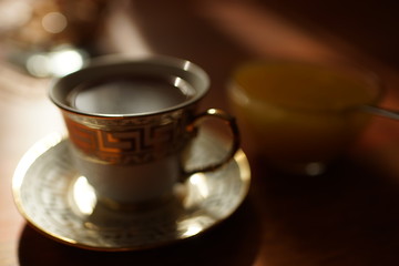 cup of tea on a saucer, cookies and honey in a vase on the table. Blurred.