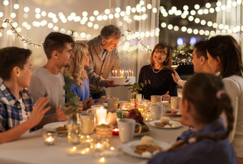 dinner party and celebration concept - happy family with cake celebrating grandmothers birthday at...