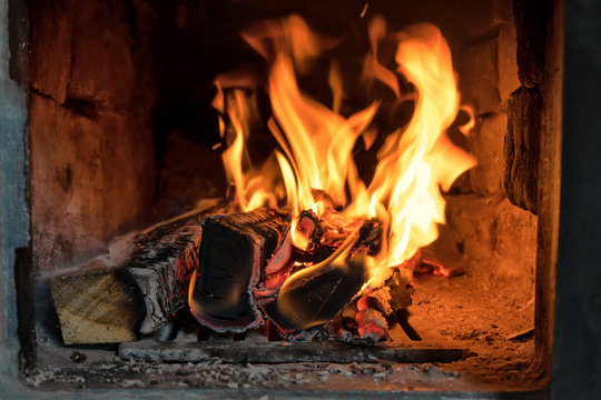 View inside an old rustic stone stove. Firewood burns in the stove. Flames rise. Background.