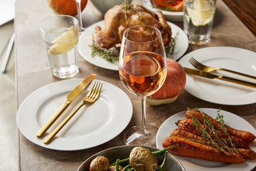 festive dinner with baked vegetables, grilled turkey and glasses with rose wine on stone table