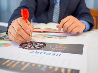 Businessman holding a darts aiming at the target center of dart board, Setting challenging business goals And ready to achieve the goal concept