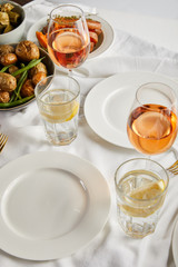 baked potatoes near glasses with rose wine and lemon water on white tablecloth