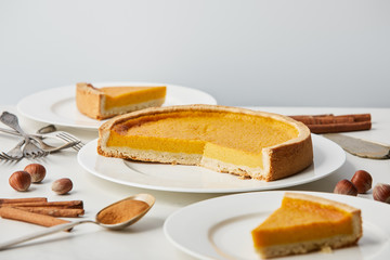white plates with tasty pumpkin pie near cutlery and spices isolated on grey