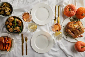 Fototapeta na wymiar top view of served thanksgiving dinner with grilled turkey, whole pumpkins and baked vegetables on white tablecloth