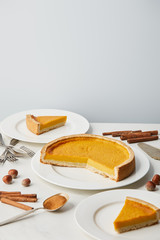 plates with tasty pumpkin pie near cutlery and spices isolated on grey