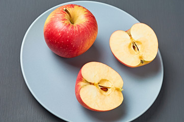 Two halves, one whole red fresh ripe apples full of vitamins lies on circle ceramic plate and old dark scratched concrete table on kitchen. Harvest or diet concept. Close-up