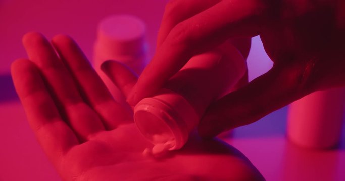 Man taking pills out of can in neon light, representing modern drug and medicine addiction - Dystopia concept close up 4k footage