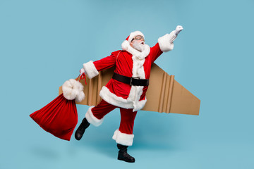 Full length body size view of his he nice fat cheerful purposeful super powerful Santa wearing plane wings flying fast delivering gifts carrying bag isolated over blue pastel color background
