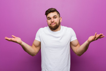Young handsome caucasian man doubting and shrugging him shoulders in questioning gesture.