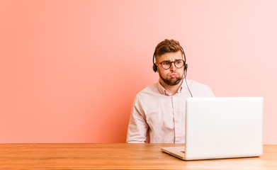 Young man working in a call center blows cheeks, has tired expression. Facial expression concept.