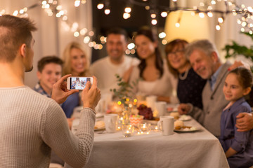 celebration, holidays and people concept - man with smartphone taking picture of family at dinner party