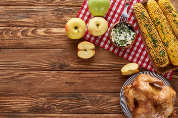 top view of roasted turkey and grilled corn served on red checkered napkin at wooden table for Thanksgiving dinner
