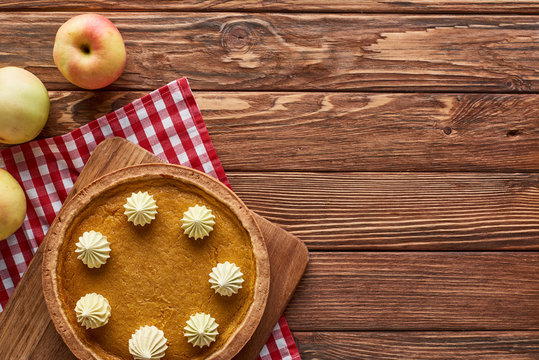 top view of pumpkin pie and apples served at wooden table with plaid napkin for Thanksgiving dinner