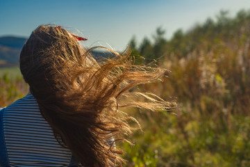 Back View of a Young Woman With Hair Blowing in the Wind While Walking in Nature on a Sunny Day