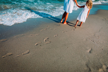 mother and daughter walking on beach leaving footprint in sand