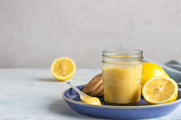A jar of lemon curd or custard with a spoon and cookies on a blue plate and fresh lemon. Selective...
