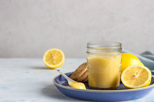 A jar of lemon curd or custard with a spoon and cookies on a blue plate and fresh lemon. Selective focus, copy space.