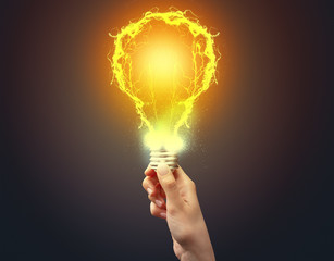 Hand holding shiny light bulb on dark background. New idea concept