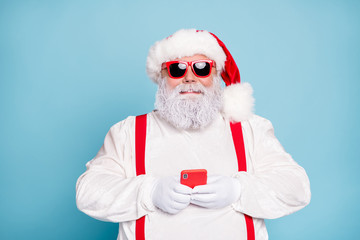 Fototapeta na wymiar Close up photo of funny funky fat white grey-haired santa claus use cell phone type sms congratulations with noel in blogs wear overalls red suspenders sunglass isolated over blue color background