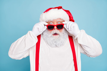 Close up photo of impressed fat overweight santa claus stare in modern eyeglasses look funny funky hear wonder christmas seasonal discounts wear suspenders overalls isolated over blue color background