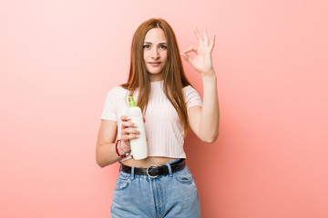 Young caucasian woman holding a cream bottle cheerful and confident showing ok gesture.