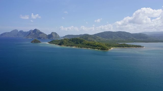 4K Aerial high attitude drone fly over ocean towards a El Nido mainland with towering limestone karst mountain ridge covered by jungle in background