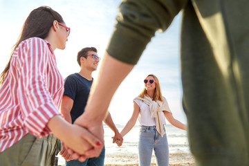 friendship, leisure and people concept - group of happy friends holding hands on beach in summer