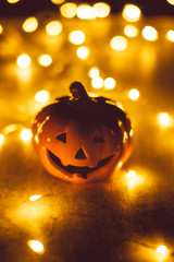 Halloween pumpkin Jack O Lantern in fairy lights for festival in Autumn with spooky dark night bokeh background.