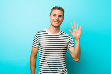 Naklejka premium Young caucasian man against a blue wall smiling cheerful showing number five with fingers.